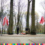 Przy pomniku stoi warta honorowa harcerzy. Widoczne drzewa i powiewające biało-czerwone flagi