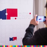 Osoba robi zdjecie telefonem komórkowym dla baneru przedstawiającego logotyp Muzeum Podlaskiego