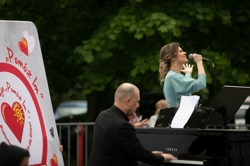 Śpiewająca kobieta, trzyma mikrofon, obok niej mężczyzna gra na fortepianie