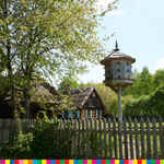 Karmnik dla ptaków widoczny za ogrodzeniem wraz z drewnianymi wiejskimi chatami