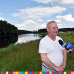 Marek Olbryś, wicemarszałek województwa podlaskiego wypowiadający się do mikrofonu telewizji. Za nim widoczna jest rzeka.
