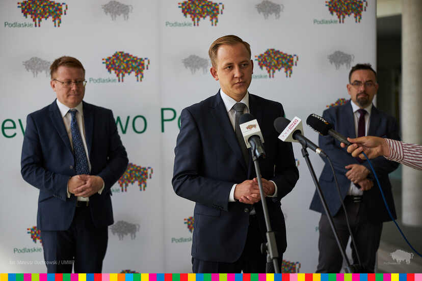 Trzech mężczyzn w trakcie konferencji. Przy mikrofonie radny Paweł Wnukowski.