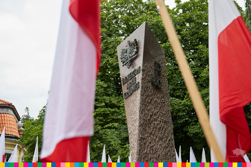 Pomnik Żołnierzy Armii Krajowej wyłaniający się między flagami biało-czerwonymi