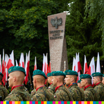 Głowy żołnierzy widoczne na zdjęciu. W tle stoi pomnik i flagi biało-czerwone