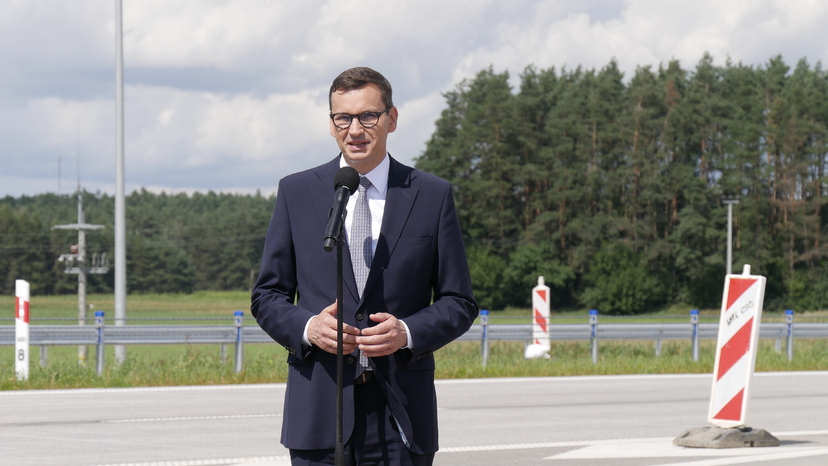 Premier Mateusz Morawiecki stoi przy mikrofonie na tle nowo oddanej do użytku drogi