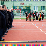 Zaproszeni goście stojący po lewej stronie na baczność oraz uczniowie świętują otwarcie kompleksu sportowego