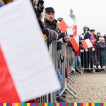 Osoby opierają się o barierki i trzymają biało-czerwone flagi w rękach