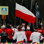 Uczestnicy biorą udział w biegu. Jeden z nich trzyma flagę biało-czerwoną, która powiewa