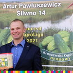 artur pawluszewicz z wiaderkiem ogorkow w reku stoi przed swoim banerem reklamowym
