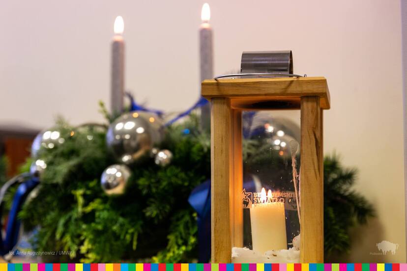 Lampion z płonącą świecą na tle stroika świątecznego.