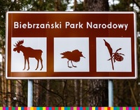 Tablica informacyjna z napisem Biebrzański Park Narodowy. Poniżej znaki: łoś, ptak i owad.