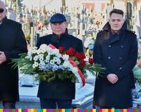 Wicemarszałek Marek Olbryś trzyma wieniec i stoi między dwoma osobami ubranymi w czarne płaszcze