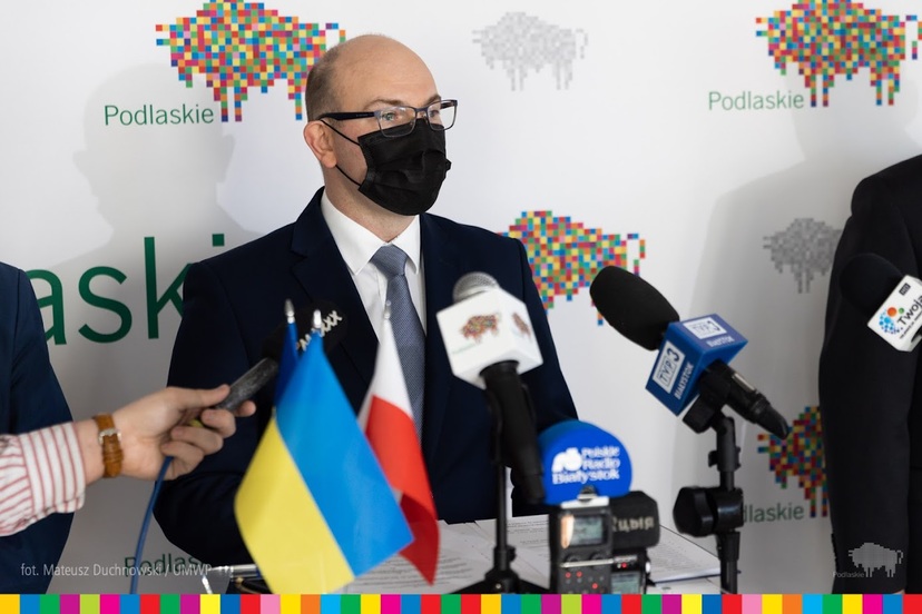 Marszałek Artur Kosicki stoi za mikrofonami na konferencji prasowej. Widoczna flaga Ukrainy oraz Polski