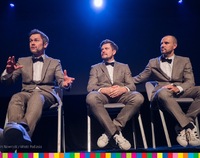 Trzech mężczyzn siedzi obok siebie w szarych garniturach i muszkach