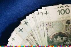 Banknoty o nominale 100 zł z profilem Władysława Jagiełły leżą na niebieskiej powierzchni ułożone w wachlarz