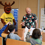 Tomasz Samojlik prowadzi warsztaty dla dzieci, obok niego stoi nowa maskotka Książnicy Podlaskiej - Łoś Czytuś