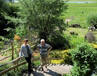 Kobieta i mężczyzna stoją na schodach prowadzących na wzgórze. W tle widoczne pole, drzewa oraz rzeka