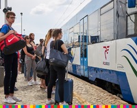Ludzie stoją z torbami na peronie przed wagonem pociągu