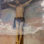 Figura Pana Jezusa ukrzyżowanego. W szybie odbijaja się niebo z chmurami