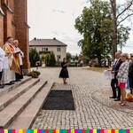 Ksiądz i ministranci stoją na stopniu przed kościołem, po prawej stronie widoczni uczestnicy z wieńcem dożynkowym