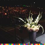 Kwiaty w wazonie ustawione na scenie, w tle uczestnicy wydarzenia siedzący na widowni