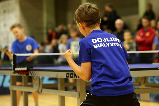 Chłopak z koszulką sportową z napisem Dojlidy Białystok gra w tennisa stołowego