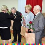 dwie kobiety oraz dwóch starszych mężczyzn składaja sobie kwiaty i upominki