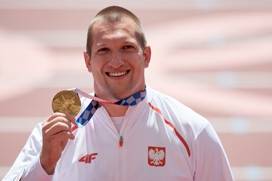 Wojciech Nowicki uśmiechnięty trzyma w dłoni złoty medal
