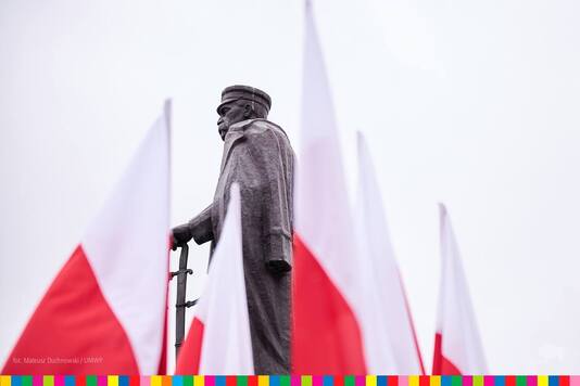 Flagi biało-czerwone. W tle pomnik Józefa Piłsudskiego